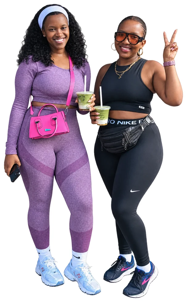 Two smiling friends in gym outfits holding iced green drinks, one of them making a peace sign